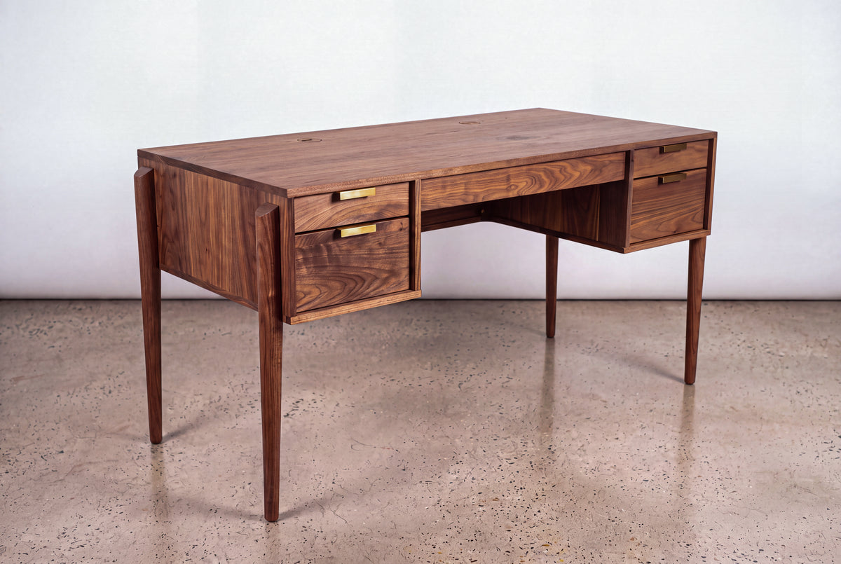 The Solid Walnut Executive Desk - Apollo Collection | TY Fine Furniture features mid-century modern design, four drawers, and brass handles—an elegant home office piece set on a polished concrete floor against a light backdrop.