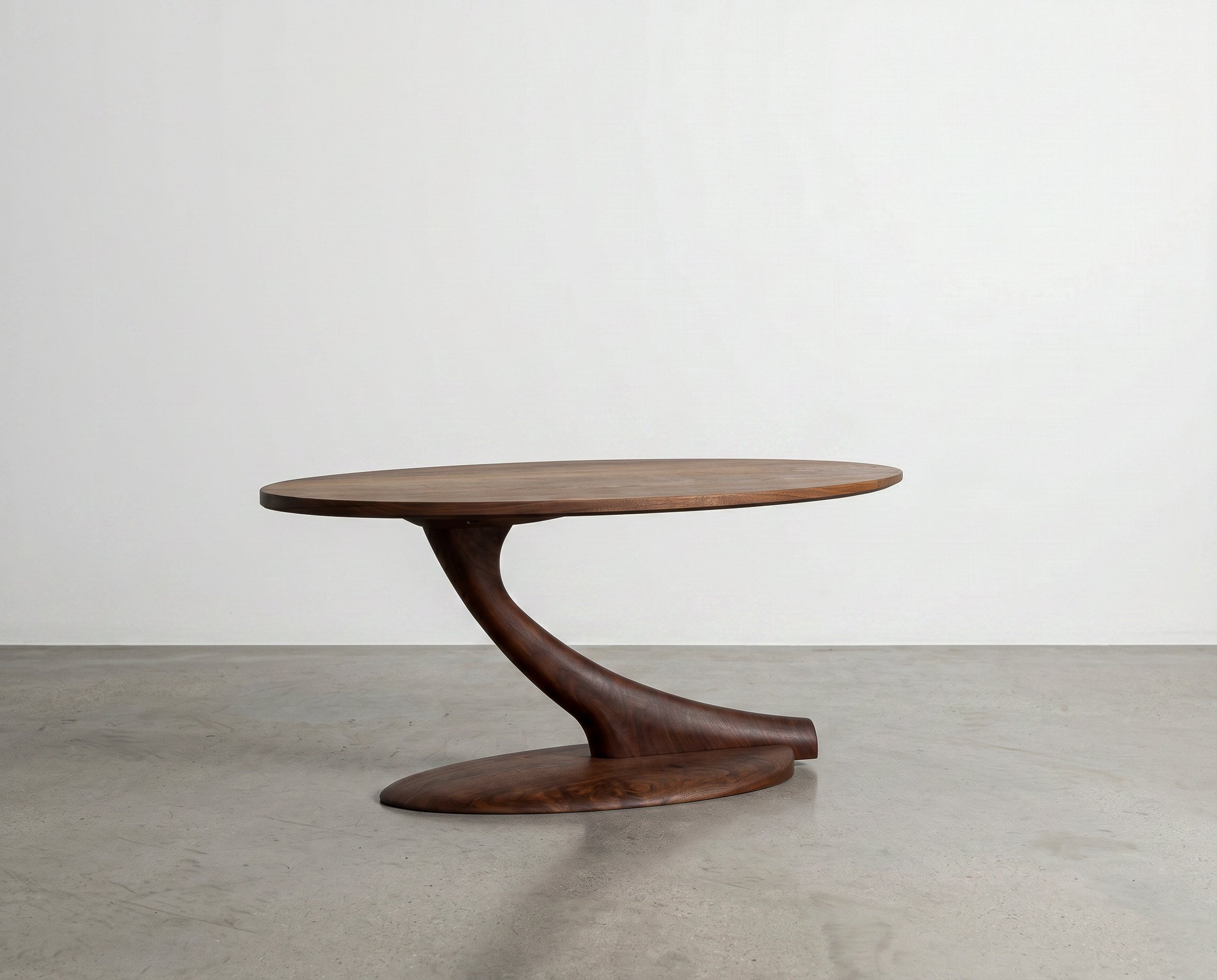 The Cantilever Oval Coffee Table Solid Wood - Maple by TY Fine Furniture features a modern design with an oval maple top and a single, elegantly twisted base that curves gracefully from the floor to support the tabletop. This handcrafted piece stands out against a plain white background on a polished concrete floor.