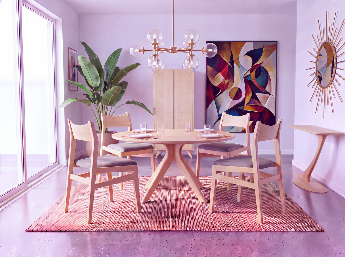 A modern dining room featuring the Solid Maple Round Dining Table from the Strata Collection by TY Fine Furniture, surrounded by four chairs, a lush plant, abstract artwork, and a sunburst mirror atop a pink rug. The handcrafted table is set with glasses and plates, while sunlight pours in through large windows.