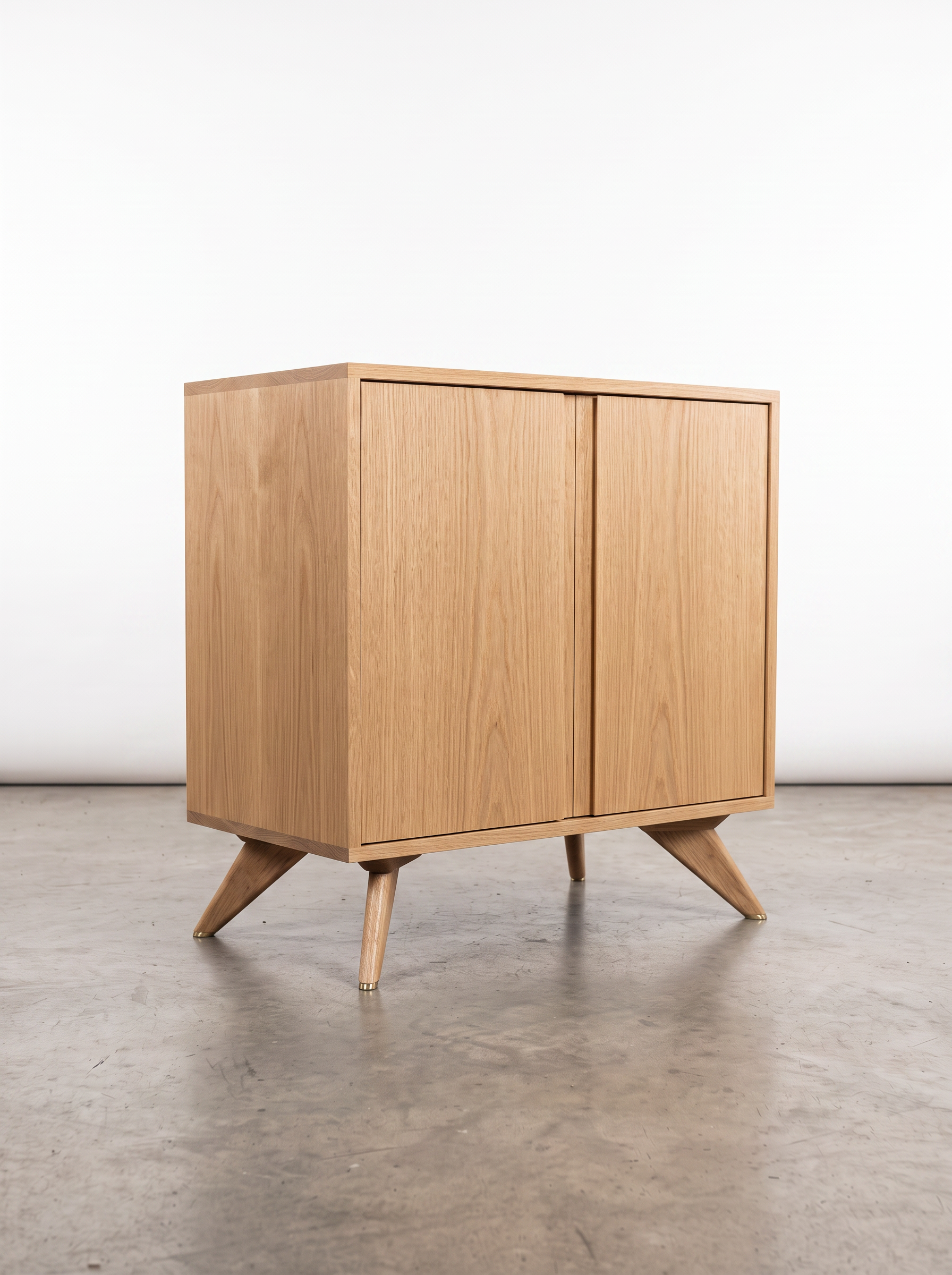 The Solid White Oak Accent Cabinet from T.Y. Fine Furniture’s Modern Collection, crafted from solid wood, features two doors and angled legs and is showcased on a polished concrete floor against a plain white background.