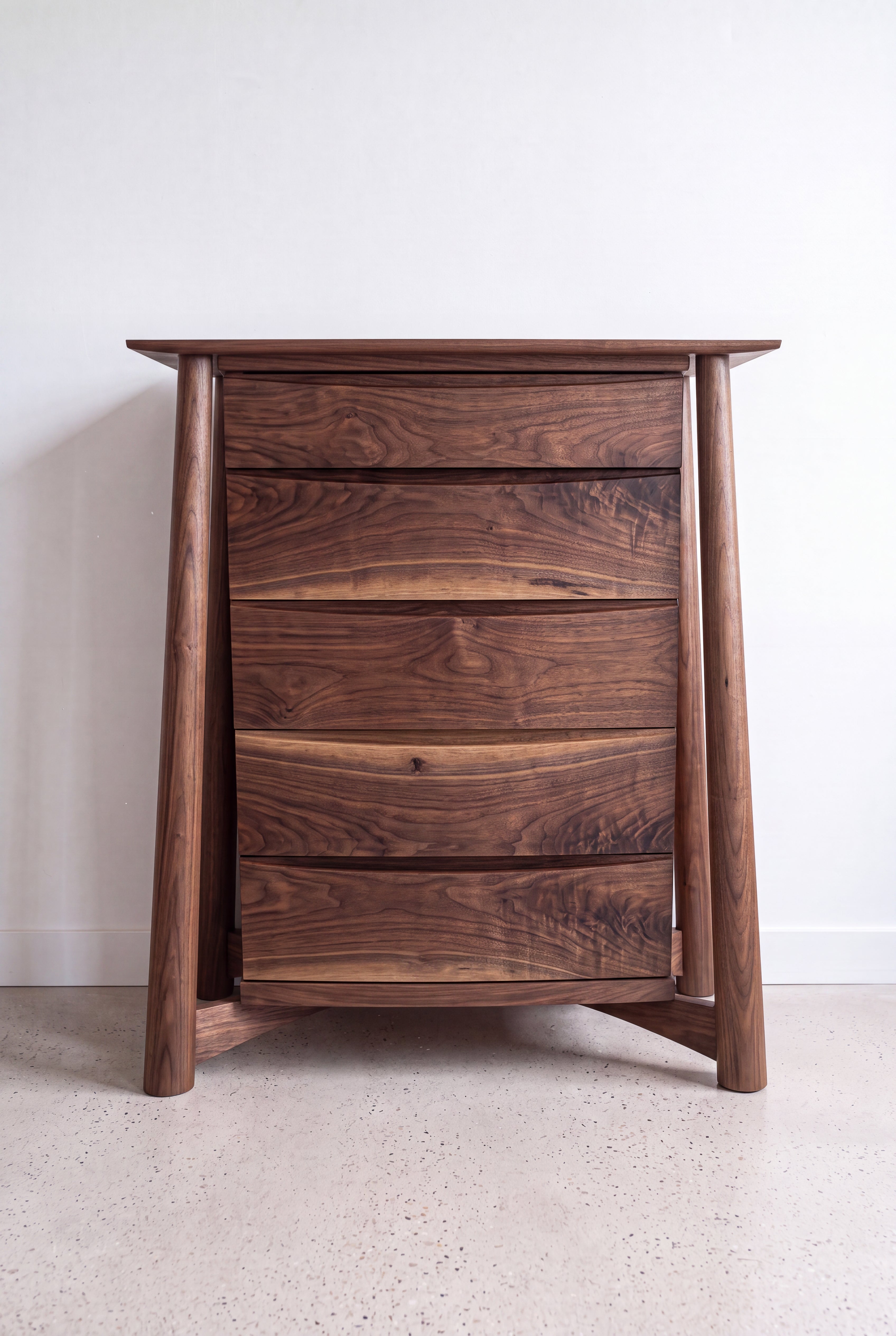 The Sunrise High Dresser by TY Fine Furniture, a solid wood maple dresser with three drawers and angled legs, is handcrafted and placed against a light-colored wall on a speckled floor.