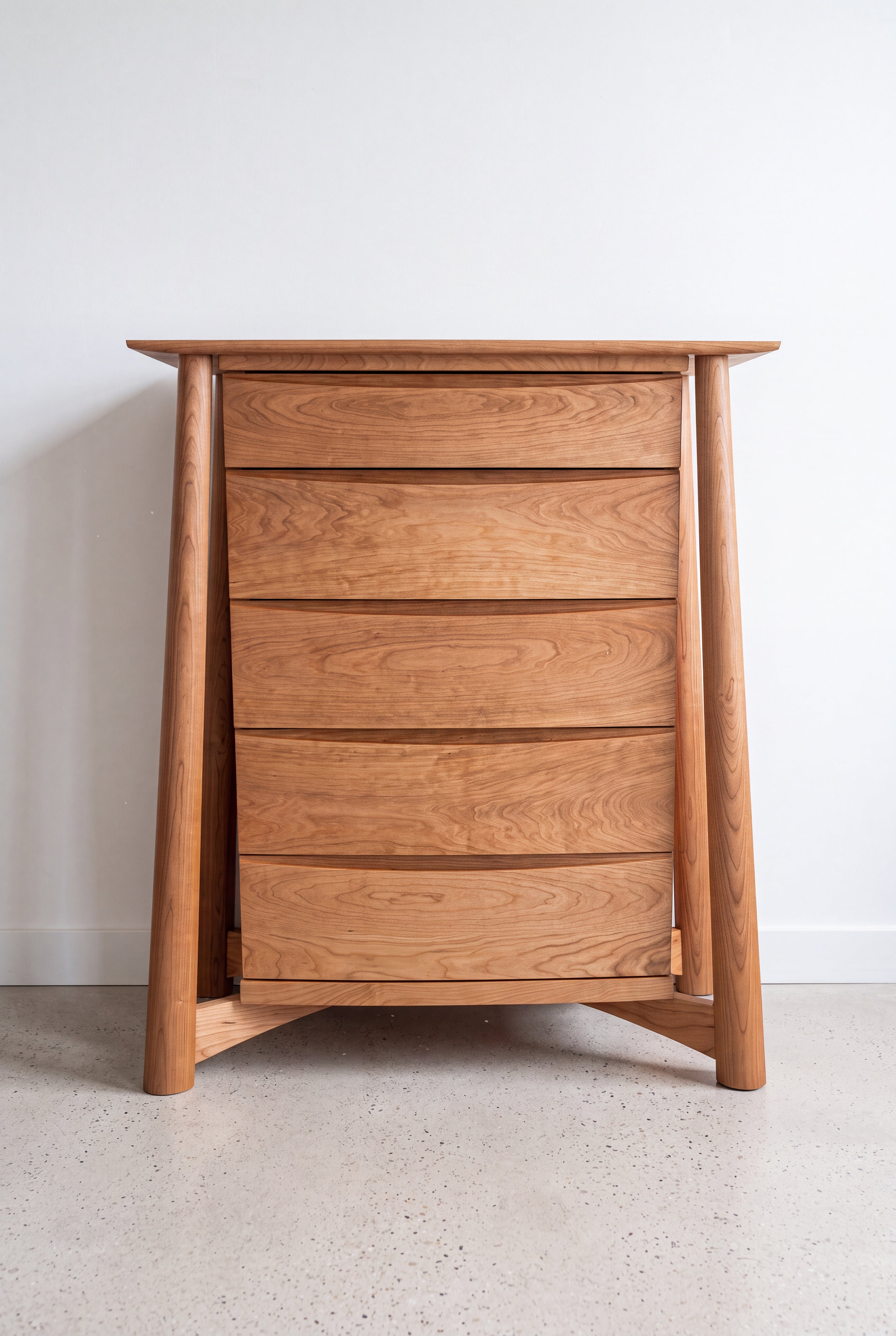 The Sunrise High Dresser by TY Fine Furniture, handcrafted from solid white oak, features four spacious drawers, elegant tapered legs, and a smooth finish. Standing on a light-colored floor against a plain white wall, this modern organic piece effortlessly combines timeless design with expert craftsmanship.