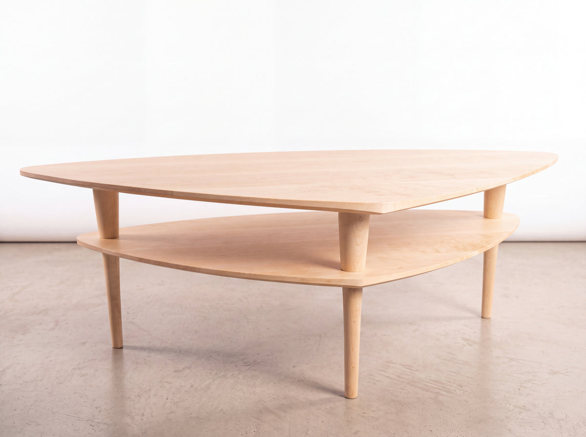 Solid Maple Coffee Table - Atomic Collection by TY Fine Furniture, a handmade mid-century piece featuring a light-colored wooden triangular top, a smaller matching lower shelf, and four tapered legs.