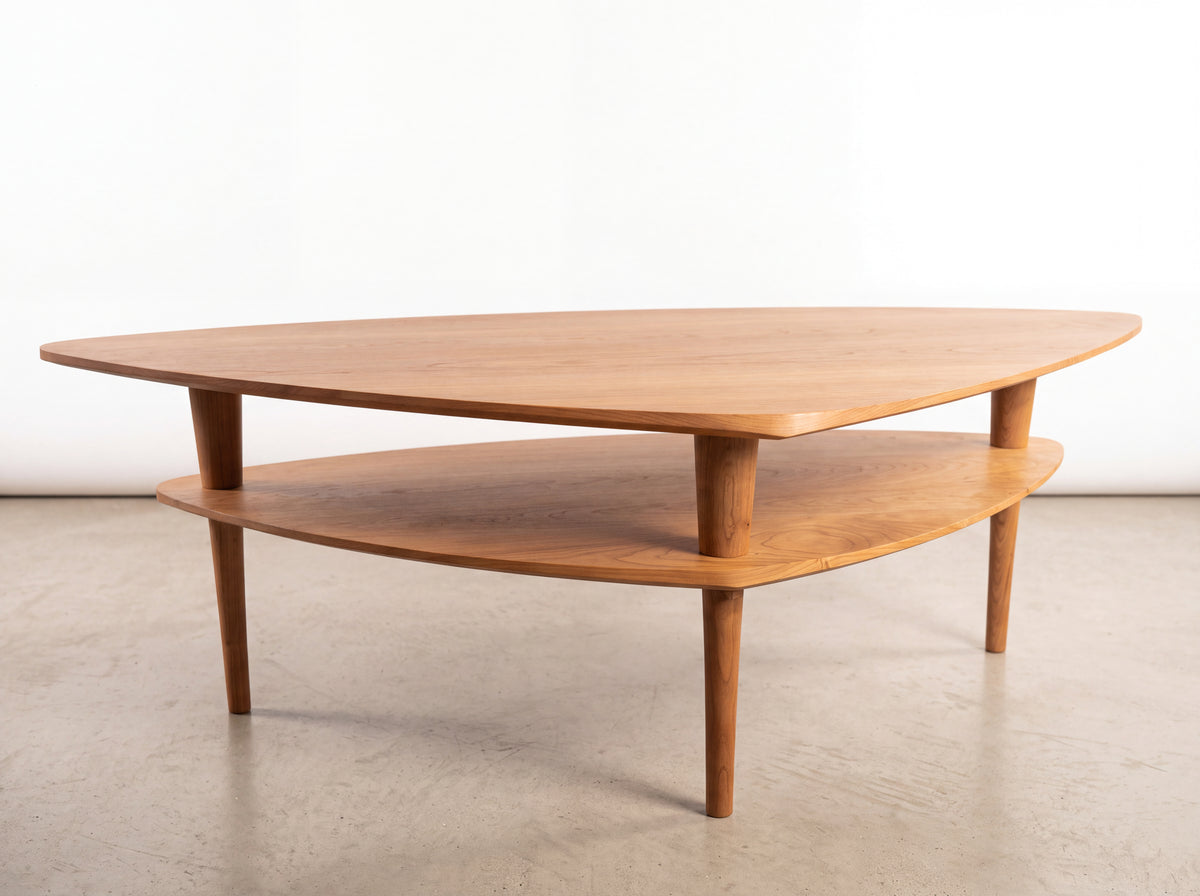 Solid Cherry Coffee Table - Atomic Collection | TY Fine Furniture, a triangular mid-century coffee table made of solid hardwood with three tapered legs and a lower shelf.