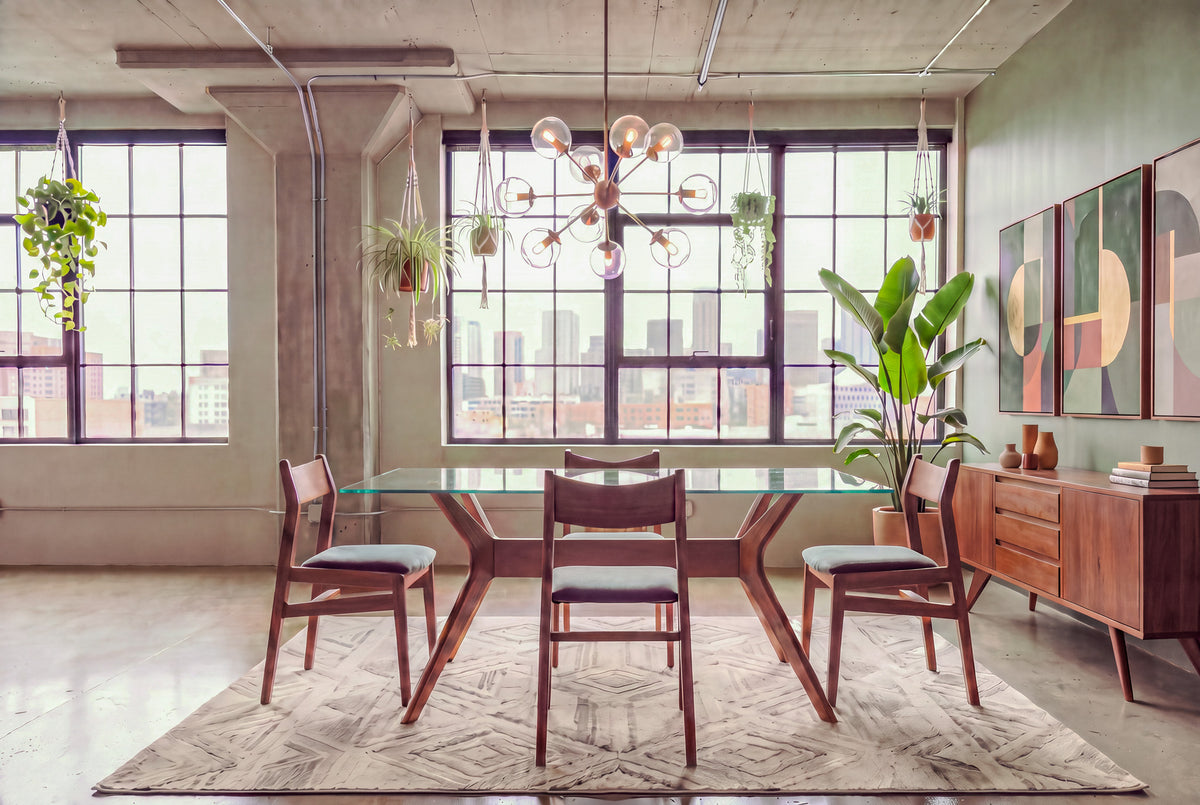 Modern dining room with large windows, mid-century wooden furniture featuring the Solid Cherry Glass-Top Dining Table from TY Fine Furniture’s Strata Collection, a geometric rug, hanging plants, a chandelier, abstract wall art, and city buildings visible outside.
