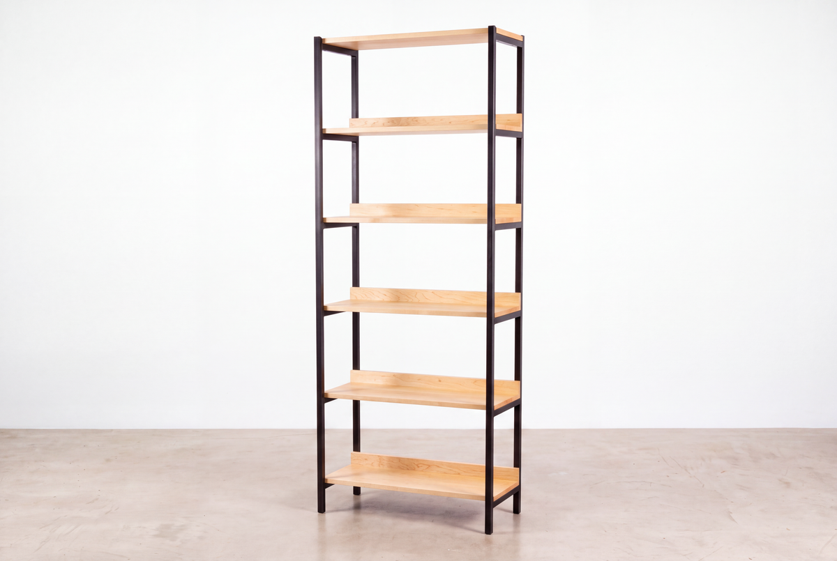 The Solid Maple Tall Mid-Century Bookcase - Essentials Collection | TY Fine Furniture features six light wood shelves and a black metal frame, standing tall on a concrete floor against a plain white wall.