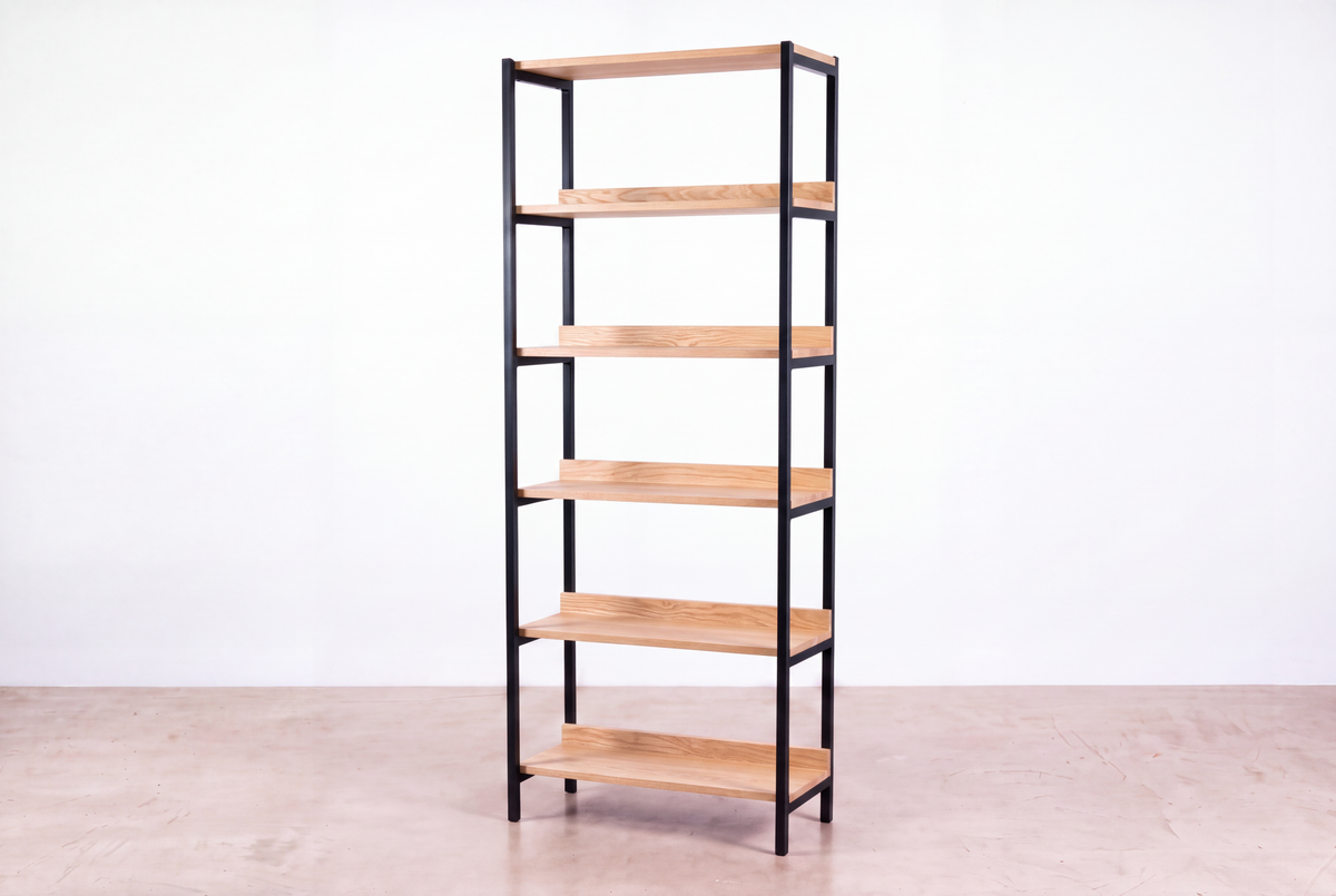 The Solid White Oak Tall Mid-Century Bookcase - Essentials Collection | TY Fine Furniture features five light wood shelves and a black metal frame, standing on a polished concrete floor against a white background.