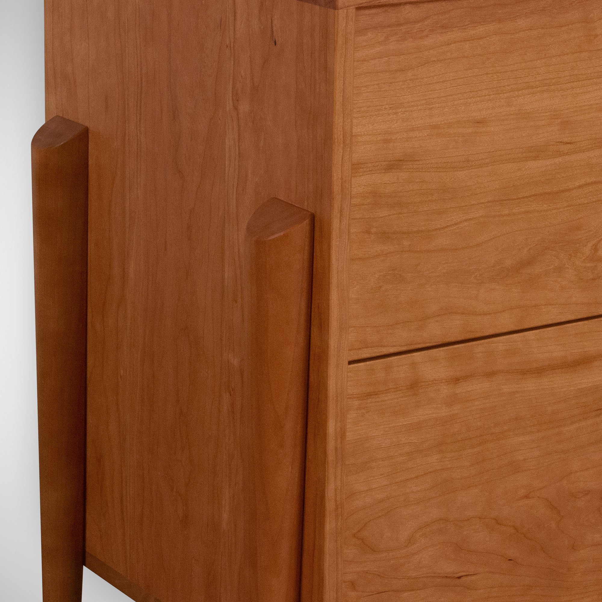 Close-up of the Apollo Dresser by TY Fine Furniture, a handcrafted Mid-Century Modern piece in cherry with smooth grain, two visible drawers, and rounded front legs. Its solid wood build and light brown finish offer stylish bedroom storage.