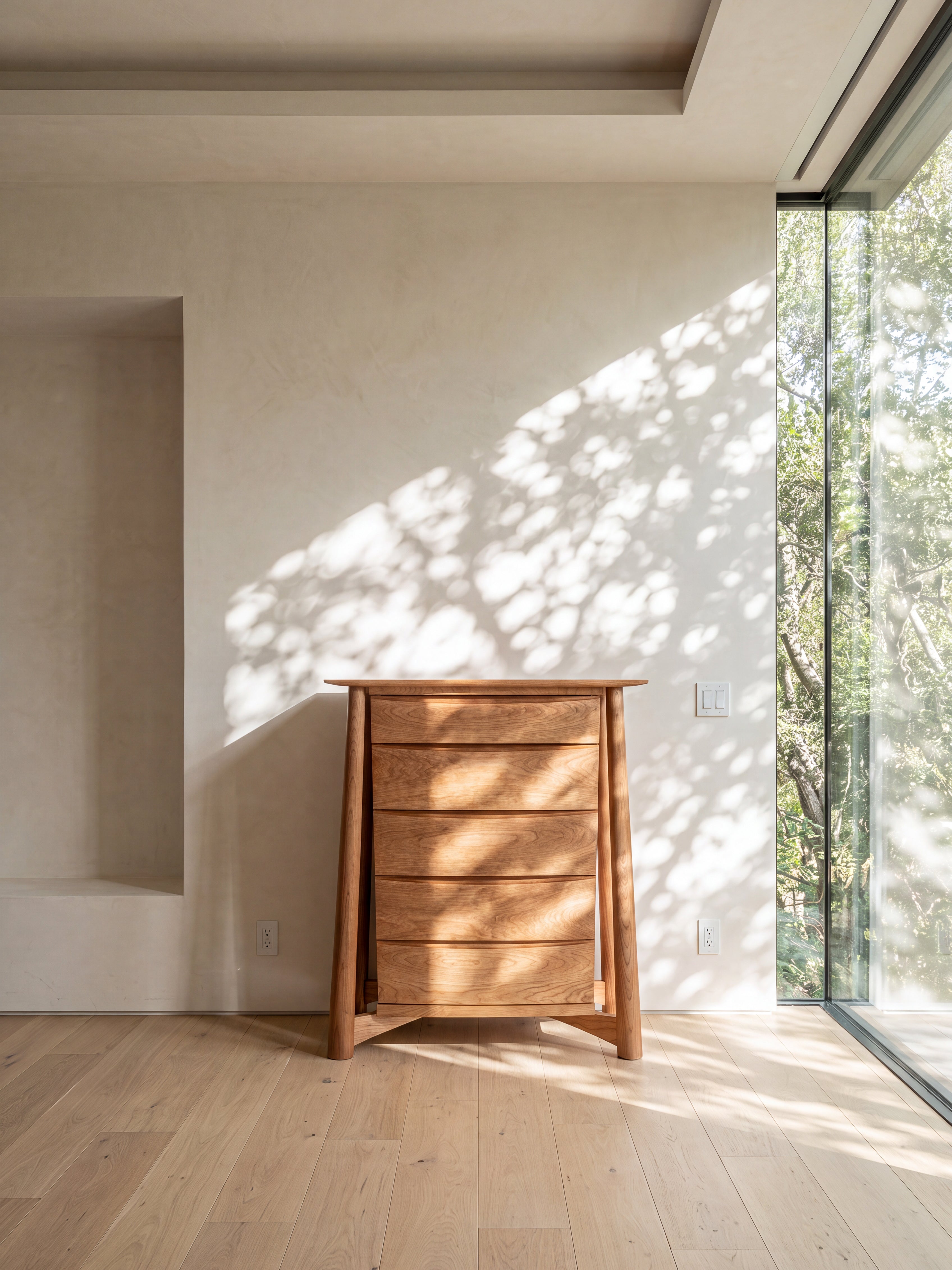 The TY Fine Furniture Sunrise High Dresser—crafted from solid cherry wood—stands against a pale wall near a large glass window, with sunlight filtering through leaves to cast dancing shadows on the wall and floor. This heirloom-quality piece brings warmth and timeless elegance to the space.