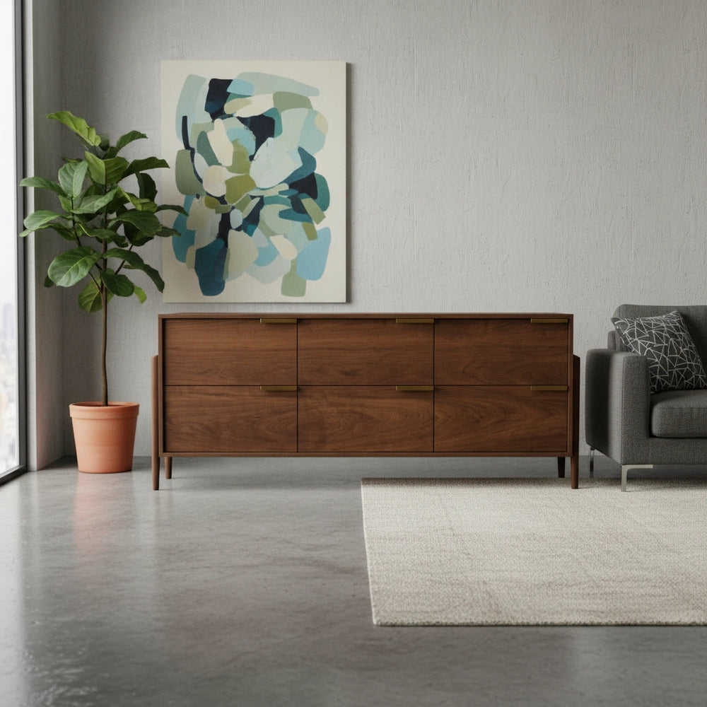 A wooden dresser with six drawers and gold handles in a room with a plant and chair