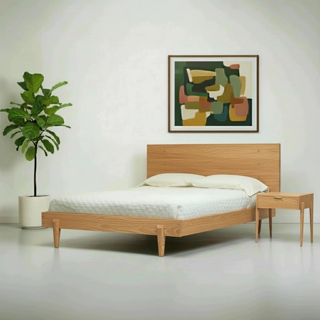 A minimalist bedroom featuring the TY Fine Furniture Apollo Platform Bed in white oak, crisp bedding, a matching wooden nightstand, a potted plant, and abstract art. The room exudes a clean, modern look with solid wood accents.