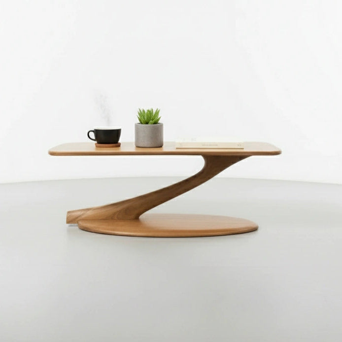 The Cantilever Coffee Table Solid Wood- Cherry by TY Fine Furniture features a modern, minimalist design with a curved base, shown with a black cup and saucer, potted plant, and book against a white background. Made in the USA.