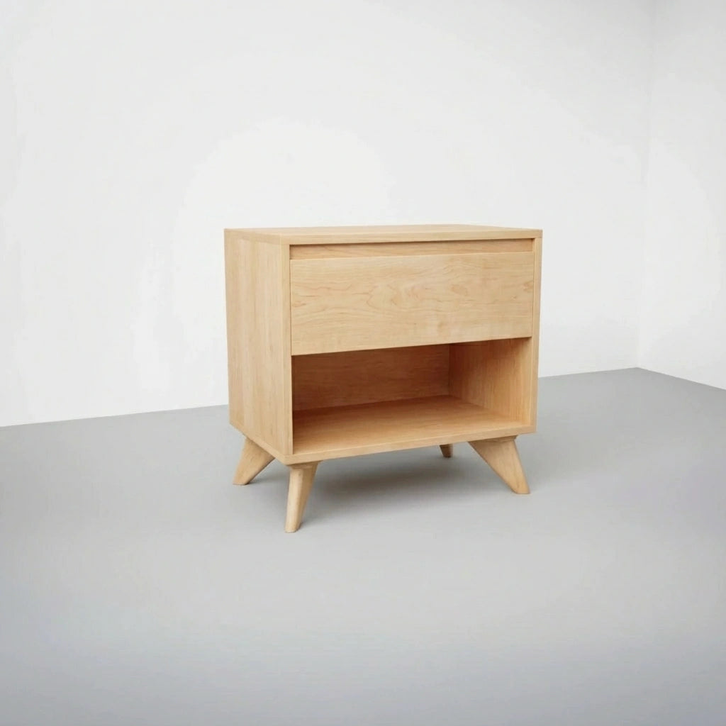 The TY Fine Furniture Modern Cube Side Table - Maple is crafted from light solid wood with angled legs, a push-to-open top drawer, and an open lower shelf, shown against a plain white wall and gray floor.