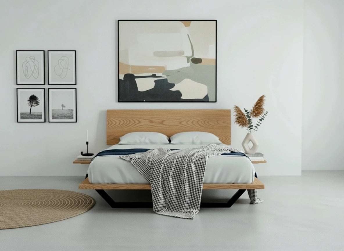 A minimalist bedroom features the TY Fine Furniture Nelson Solid Wood Platform Bed Frame in American White Oak, white and gray bedding, abstract art above, a pampas grass vase on the side, four black-and-white photos, and a round rug for a cozy finish.